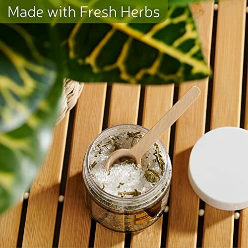 Jar of herbal bath salts with wooden spoon on wooden surface.